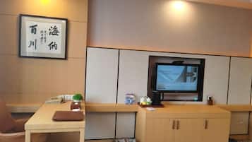 A hotel room with a wooden desk, a television, a framed picture on the wall, and a trash bin.