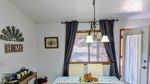 Un coin repas avec une table dressée pour deux personnes, un lustre et une vue par la fenêtre.