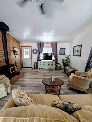 A living room with a fireplace, sofa, coffee table, and a TV. - Warm & Relaxing Home, Pet Friendly and Full Fenced Yard. (Lakeside)