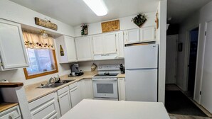 Une cuisine avec des meubles blancs, un îlot central, un réfrigérateur et une cuisinière.