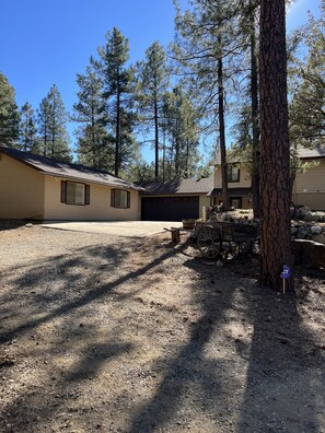 A residential area with two single-story houses, a gravel driveway, and a wooden cart.