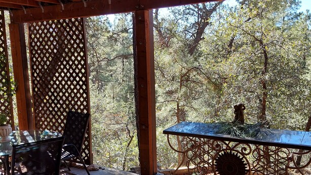 A covered patio area with a table and chairs, a decorative metal railing, and a view of trees. - 3 Room Cozy Suite in the Pines, near Downtown Prescott & many other attractions (Prescott)