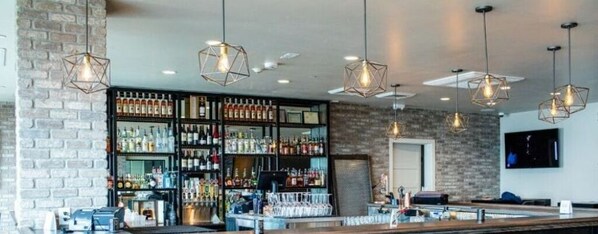 Zona de bar con pared de ladrillo, lámparas colgantes y estanterías llenas de botellas.