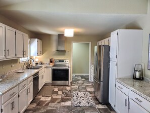 A kitchen with white cabinets, a stainless steel refrigerator, an oven, and a patterned rug.