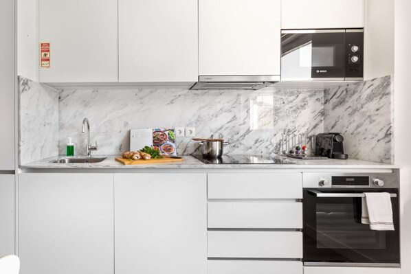 Une cuisine moderne avec des meubles blancs, un four à micro-ondes de marque Bosch, un évier et une cuisinière.