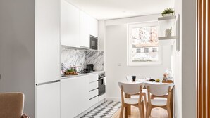 A compact kitchen with white cabinets, a marble backsplash, and a dining area with two chairs and a small table.