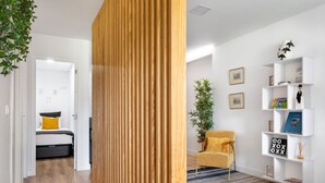 A modern living room with a wooden partition, a yellow armchair, a bookshelf, and a bed in the background.