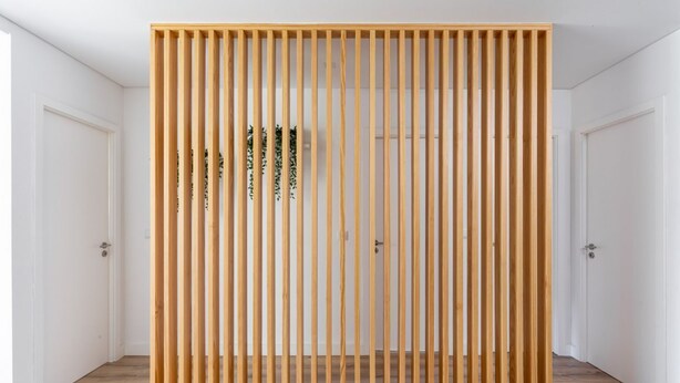 A room with a wooden slat partition, white doors, and a wooden floor.