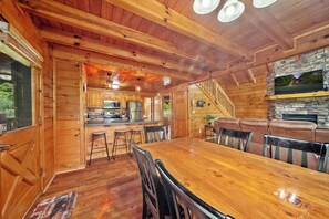 Interior de una cabaña de madera con comedor, cocina y chimenea de piedra.
