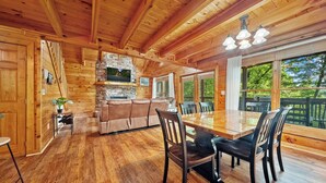 Interno di una baita in legno con zona pranzo, divano e camino in pietra.