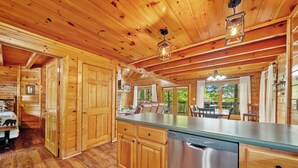 Interno di una baita in legno con cucina, caratterizzata da mobili in legno, lavastoviglie in acciaio inossidabile e zona pranzo con tavolo e sedie.