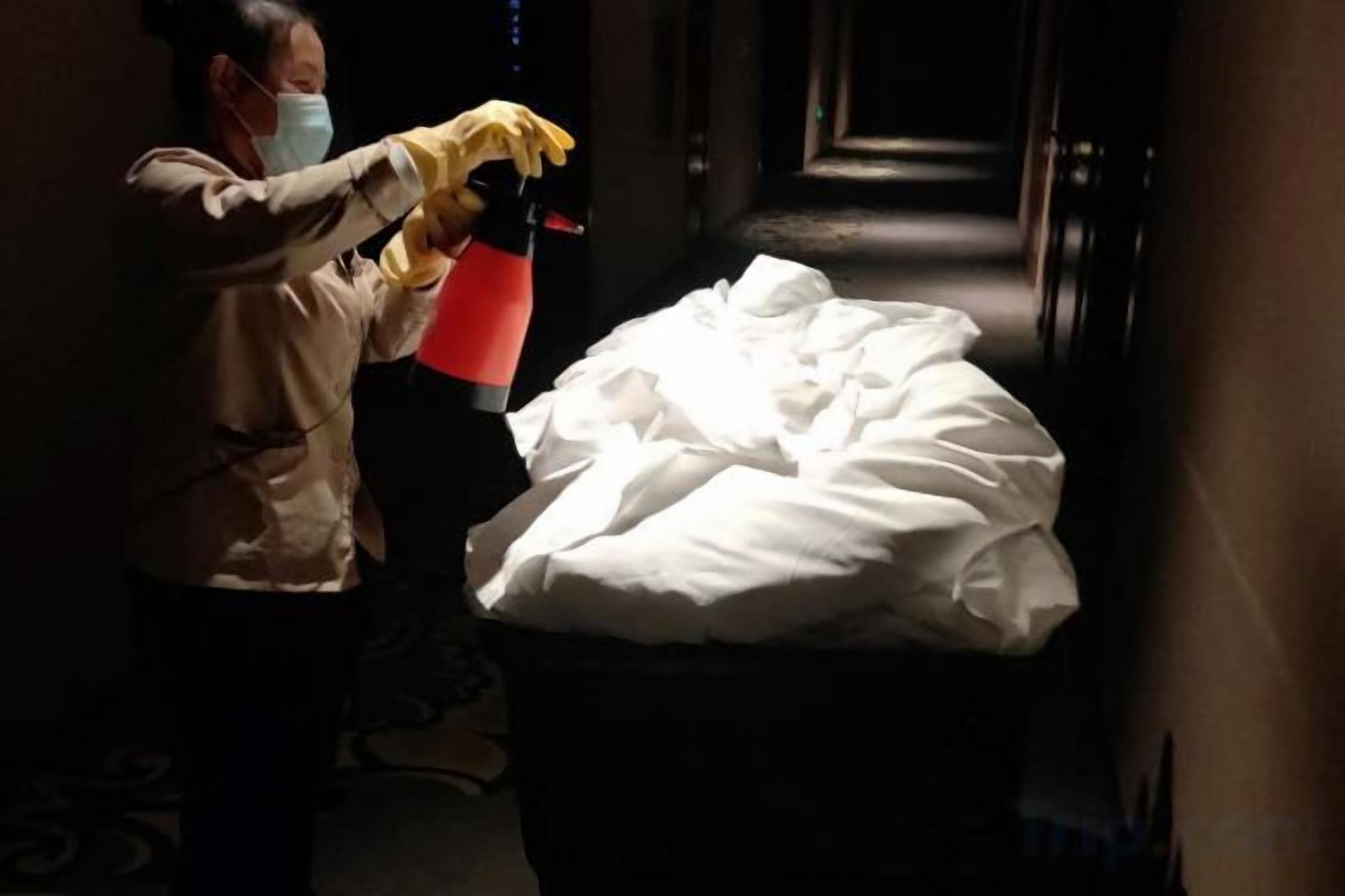 Una persona limpia una cama con un atomizador en un pasillo estrecho.