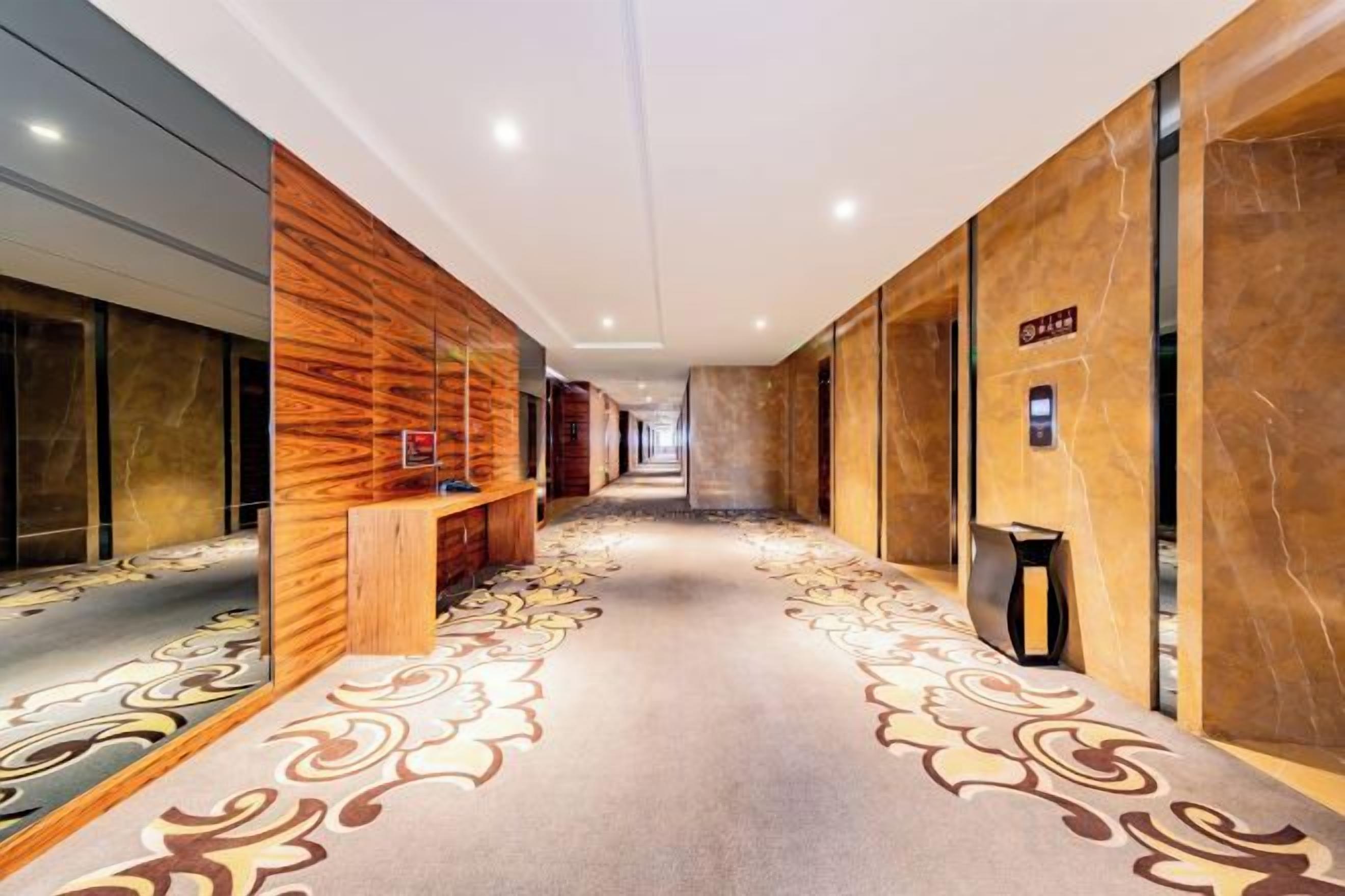A hotel corridor with a patterned carpet, wooden wall panels, and a bench.