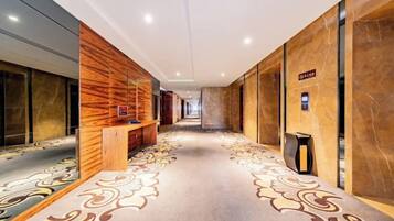 A hotel corridor with a patterned carpet, wooden wall panels, and a bench.
