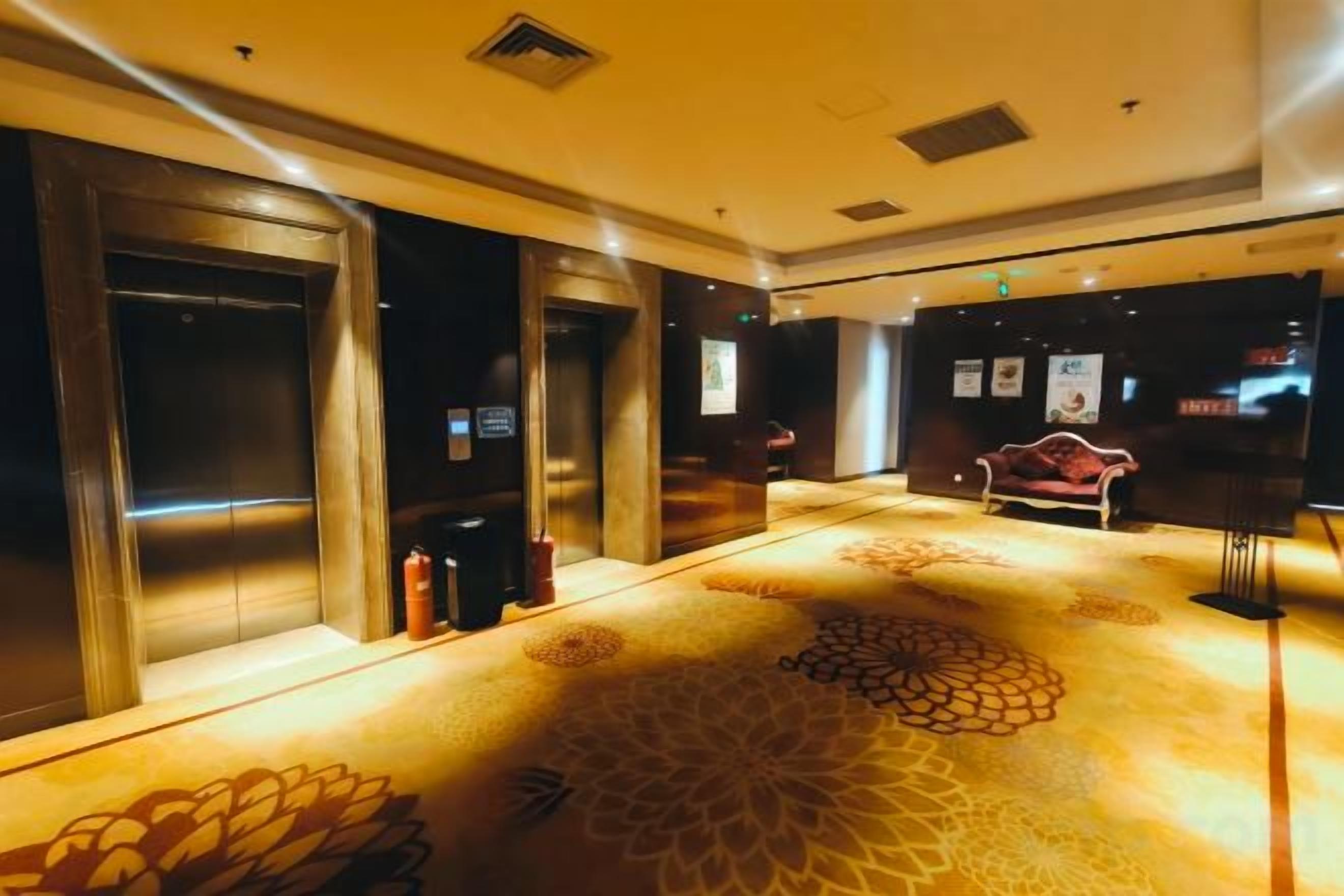 Un vestíbulo de hotel con ascensores, una alfombra estampada y un sofá rojo.