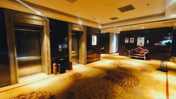 A hotel lobby with elevators, a patterned carpet, and a red sofa.