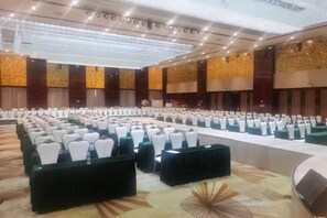 A large conference room with rows of tables and chairs, a stage, and a high ceiling with lighting fixtures. - Triumphal Gate Holiday Hotel (Toketo No.1 Middle School) (Togtoh County)