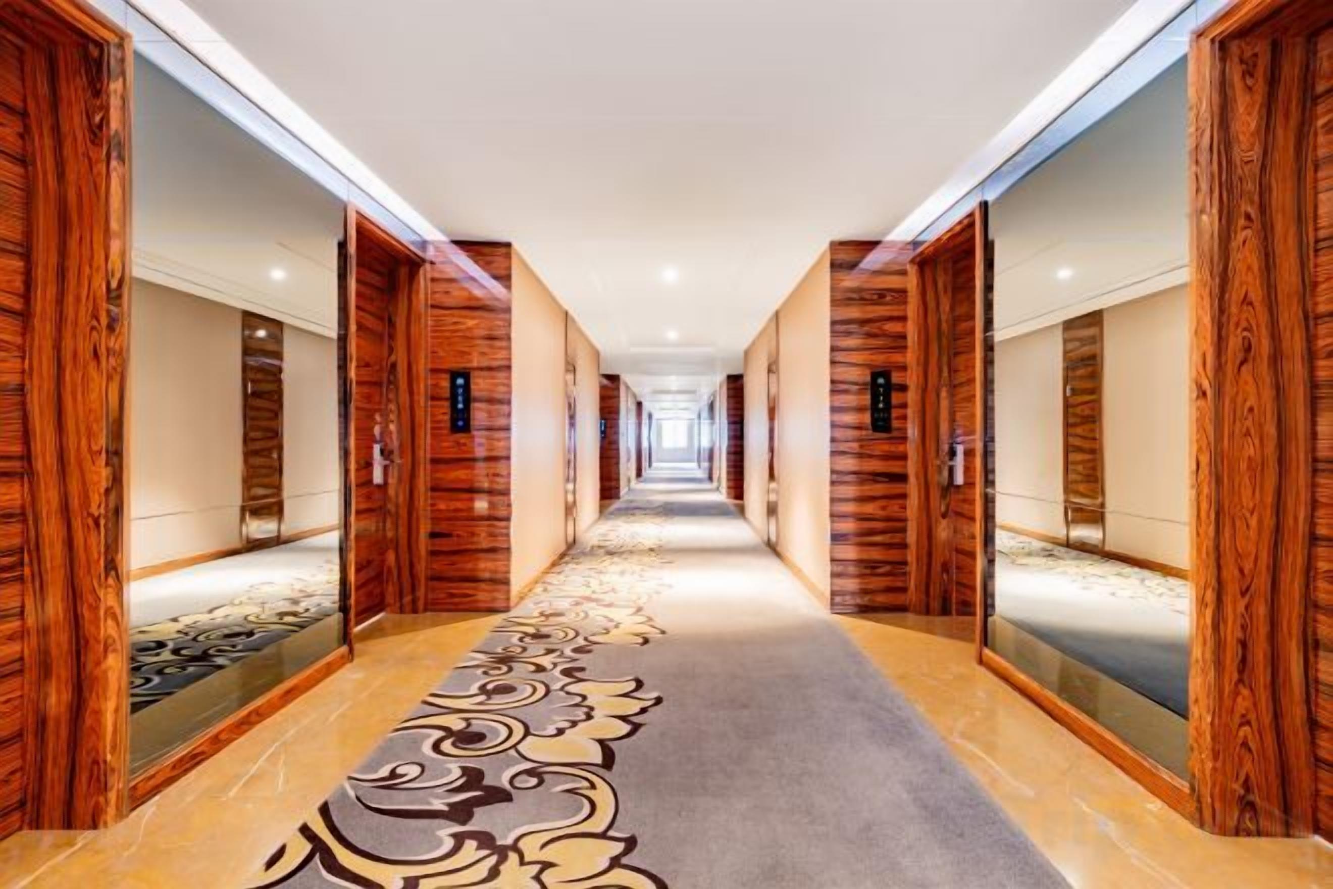 Un couloir d’hôtel avec des boiseries, une moquette à motifs et des murs recouverts de miroirs.