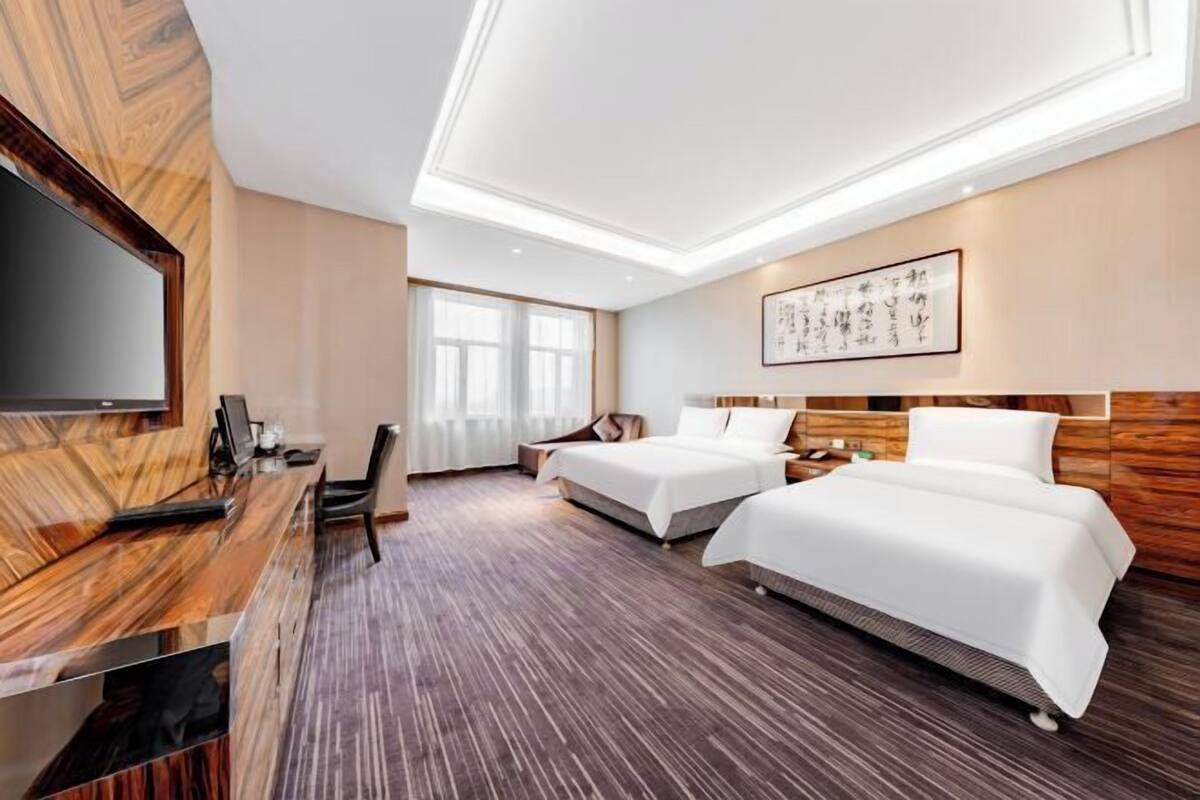 A hotel room with two beds, a desk with a computer, a TV, and a large window.