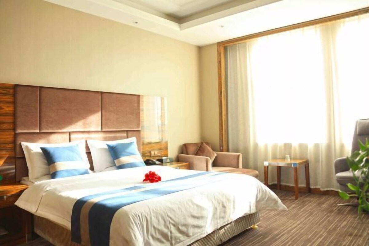 Ein Hotelzimmer mit einem großen Bett, einem hölzernen Kopfteil, einem kleinen Tisch, einem Stuhl und einem großen Fenster mit Vorhängen.