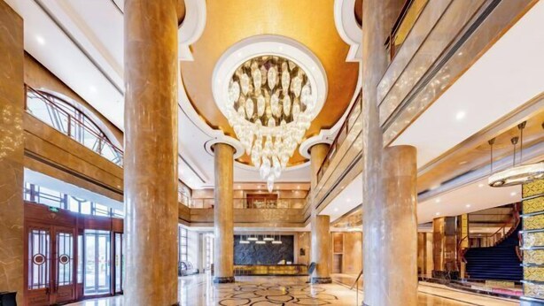 Un lobby imponente con columnas de mármol, un gran candelabro y una escalera.