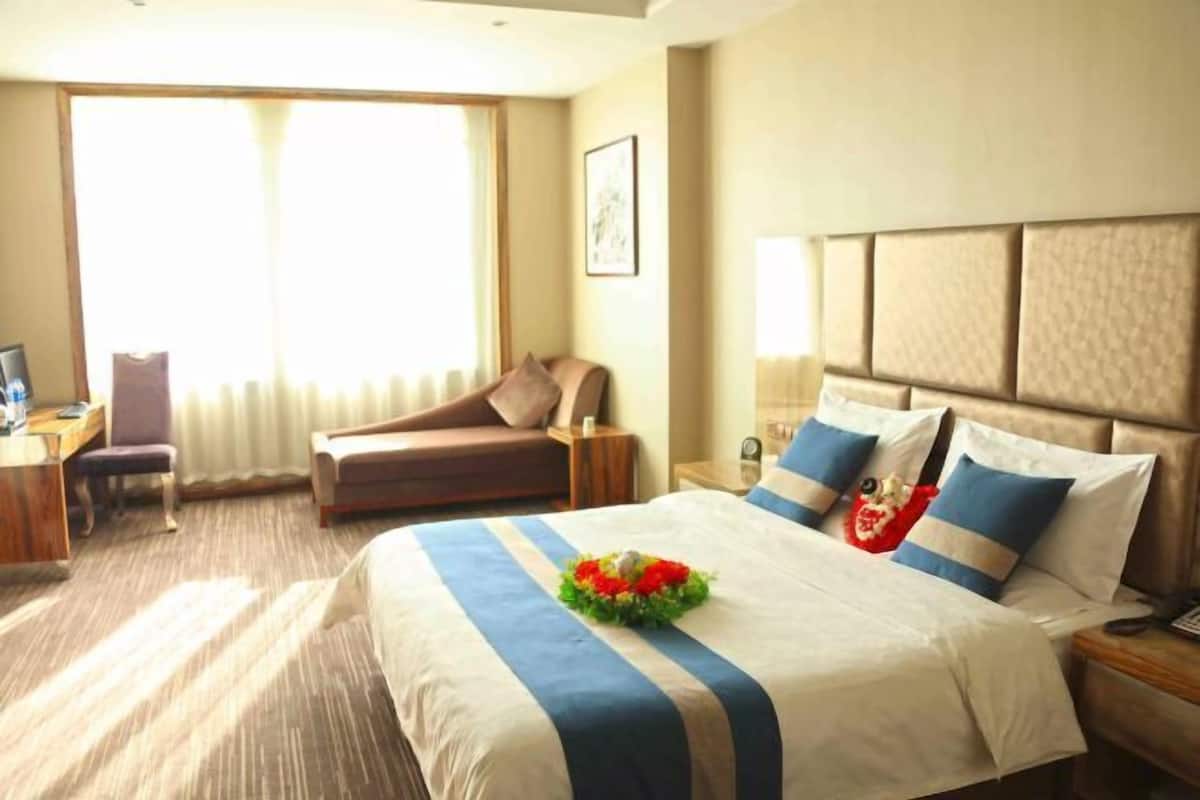 A hotel room with a large bed, a desk with a chair, a sofa, and a window with curtains.