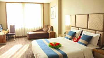 Habitación de hotel con una cama grande, un escritorio con una silla, un sofá y una ventana con cortinas.