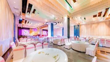 A banquet hall with round tables, white chairs, and a stage area.