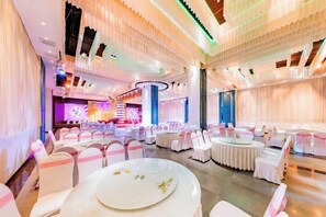 A banquet hall with round tables, white chairs, and a stage area. - Triumphal Gate Holiday Hotel (Toketo No.1 Middle School) (Togtoh County)
