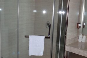 A modern bathroom with a glass shower enclosure, a towel rack with a white towel, and a marble countertop with toiletries.