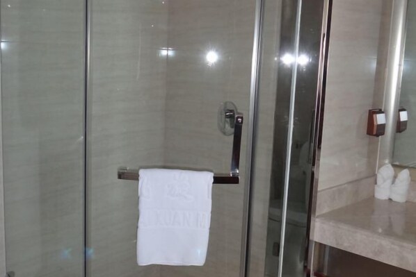 Ein modernes Badezimmer mit einer Duschkabine aus Glas, einem Handtuchhalter mit einem weißen Handtuch und einer Marmorplatte mit Toilettenartikeln.