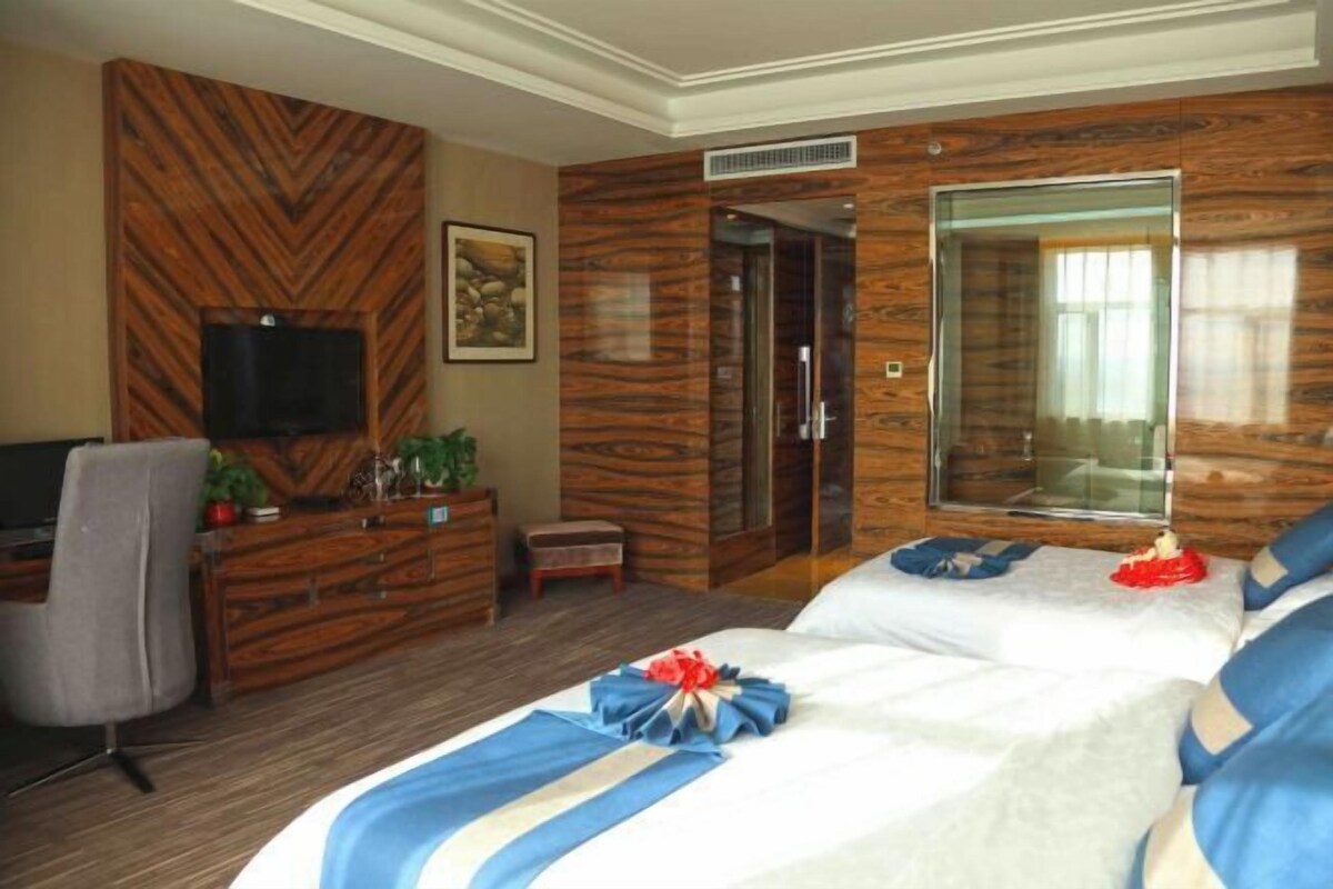 Ein Hotelzimmer mit einem großen Bett, einem an der Wand montierten Fernseher, einer Holzkommode und einem Spiegel.