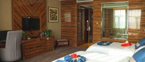 Quarto de hotel com uma cama grande, televisão na parede, cómoda de madeira e espelho.
