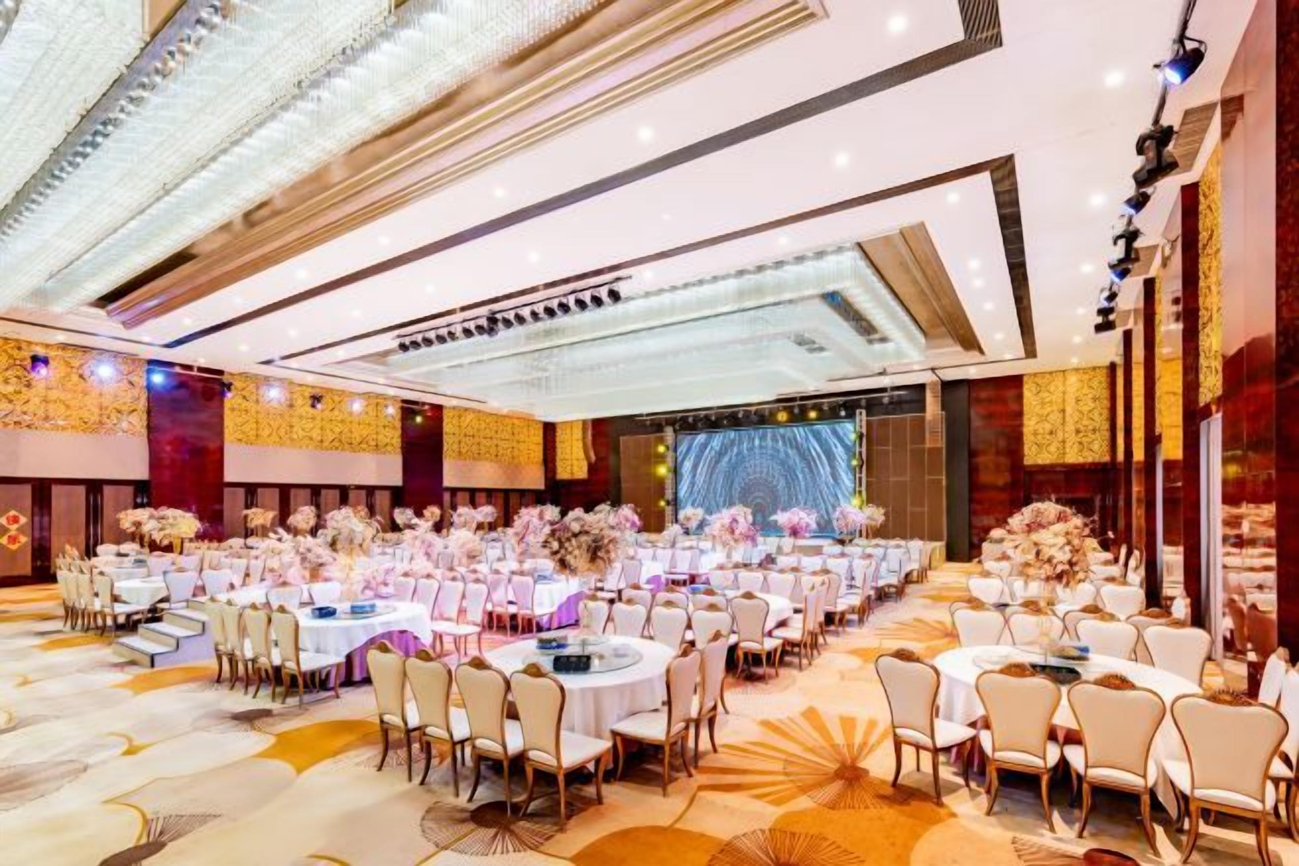A banquet hall with round tables and chairs, a stage, and a large screen.