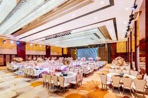 Un salón de banquetes con mesas redondas y sillas, un escenario y una gran pantalla.