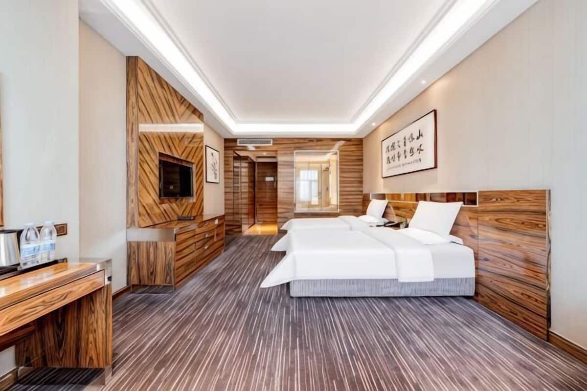 A hotel room with a wooden accent wall, a flat-screen TV, a desk, and two beds.