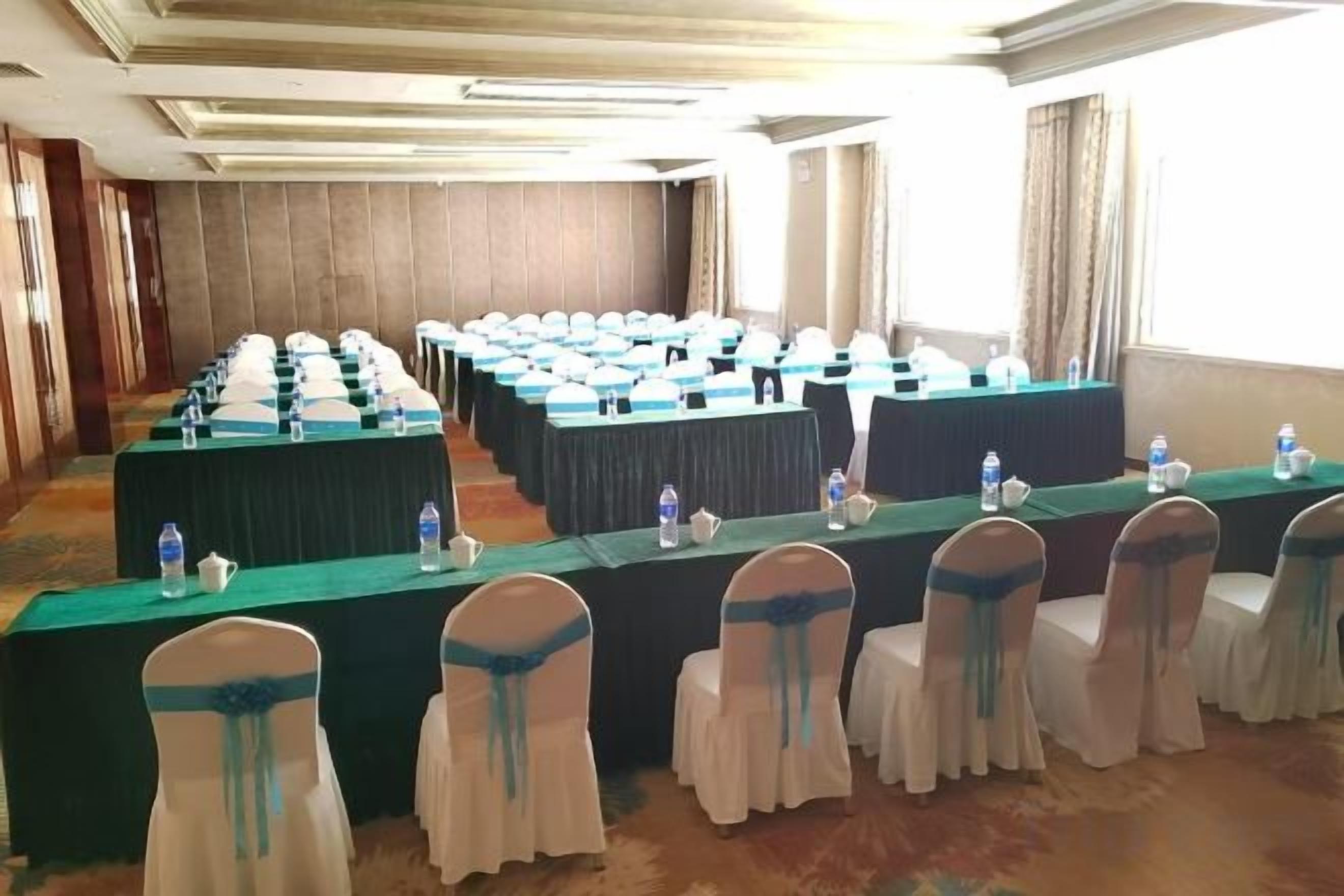 Un salón de conferencias con mesas largas, sillas y botellas de agua.