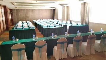 Un salón de conferencias con mesas largas, sillas y botellas de agua.