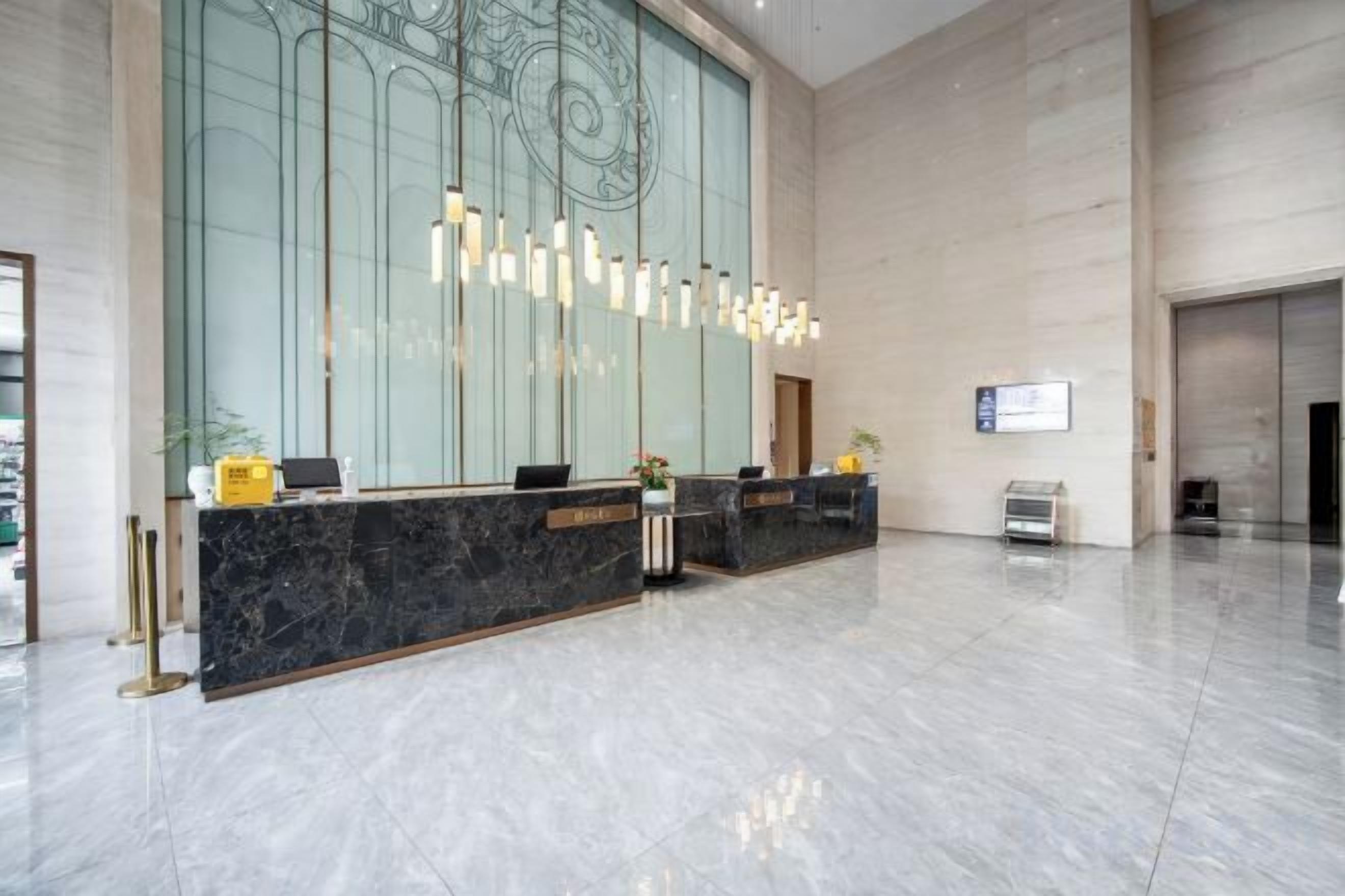 Zona de recepción de hotel con mostrador de mármol, iluminación colgante moderna y un amplio ventanal.
