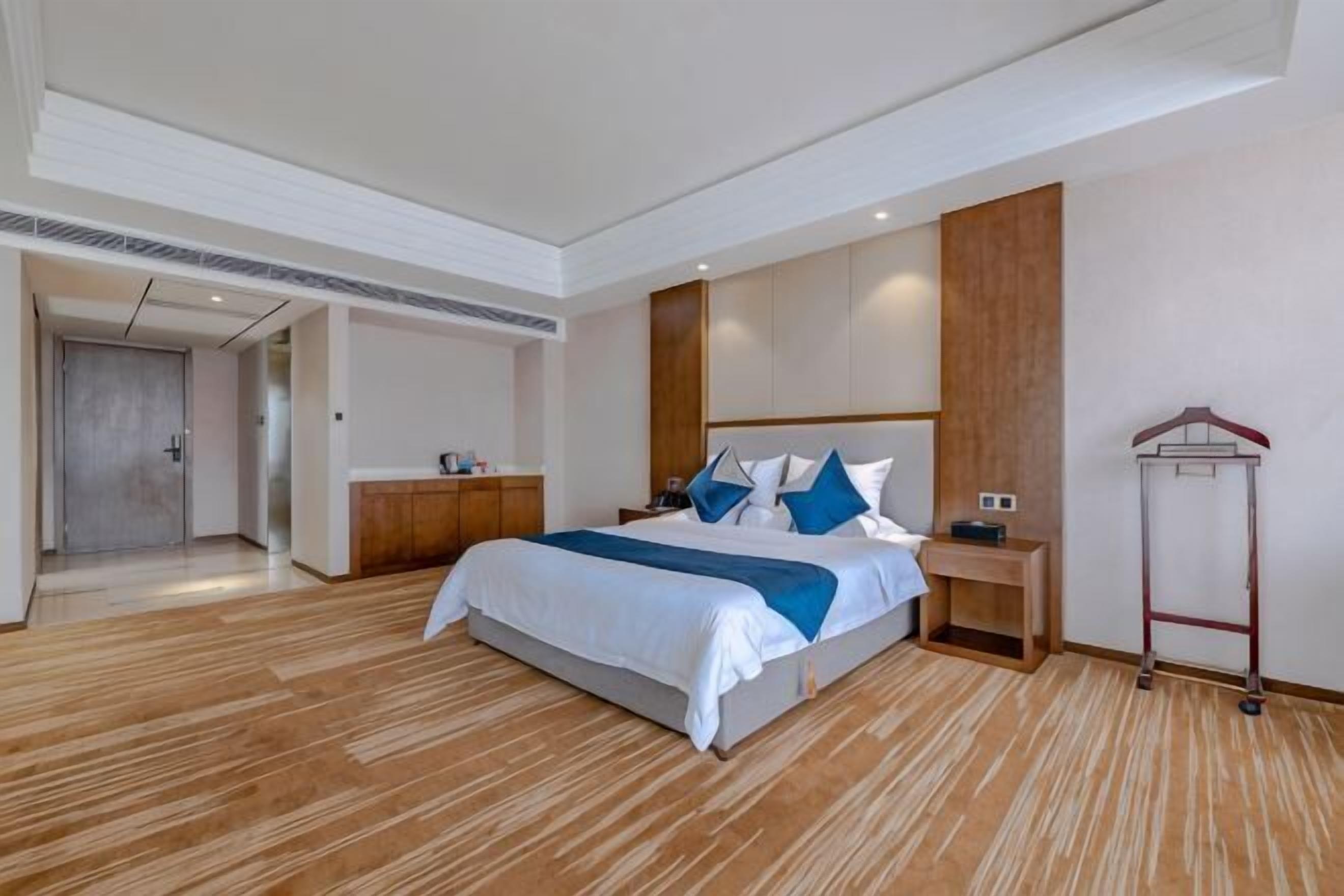 A hotel room with a large bed, wooden flooring, a wardrobe, a bedside table, and a coat rack.