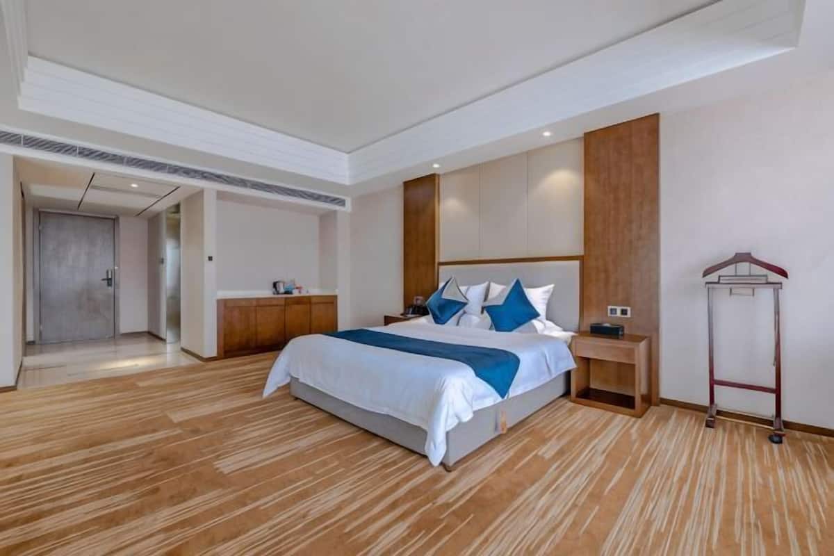 A hotel room with a large bed, wooden flooring, a wardrobe, a bedside table, and a coat rack.