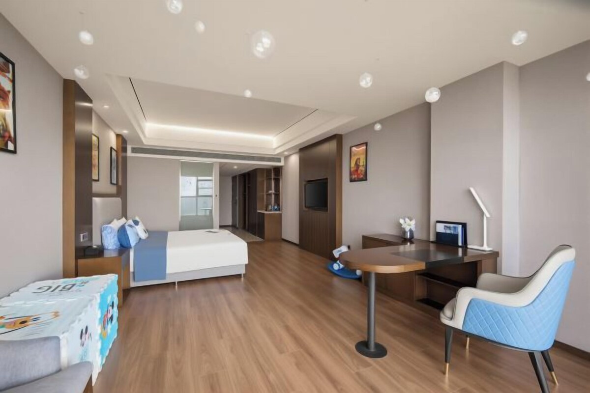 Een moderne hotelkamer met een bed, bureau, stoel en een klein zithoekje.
