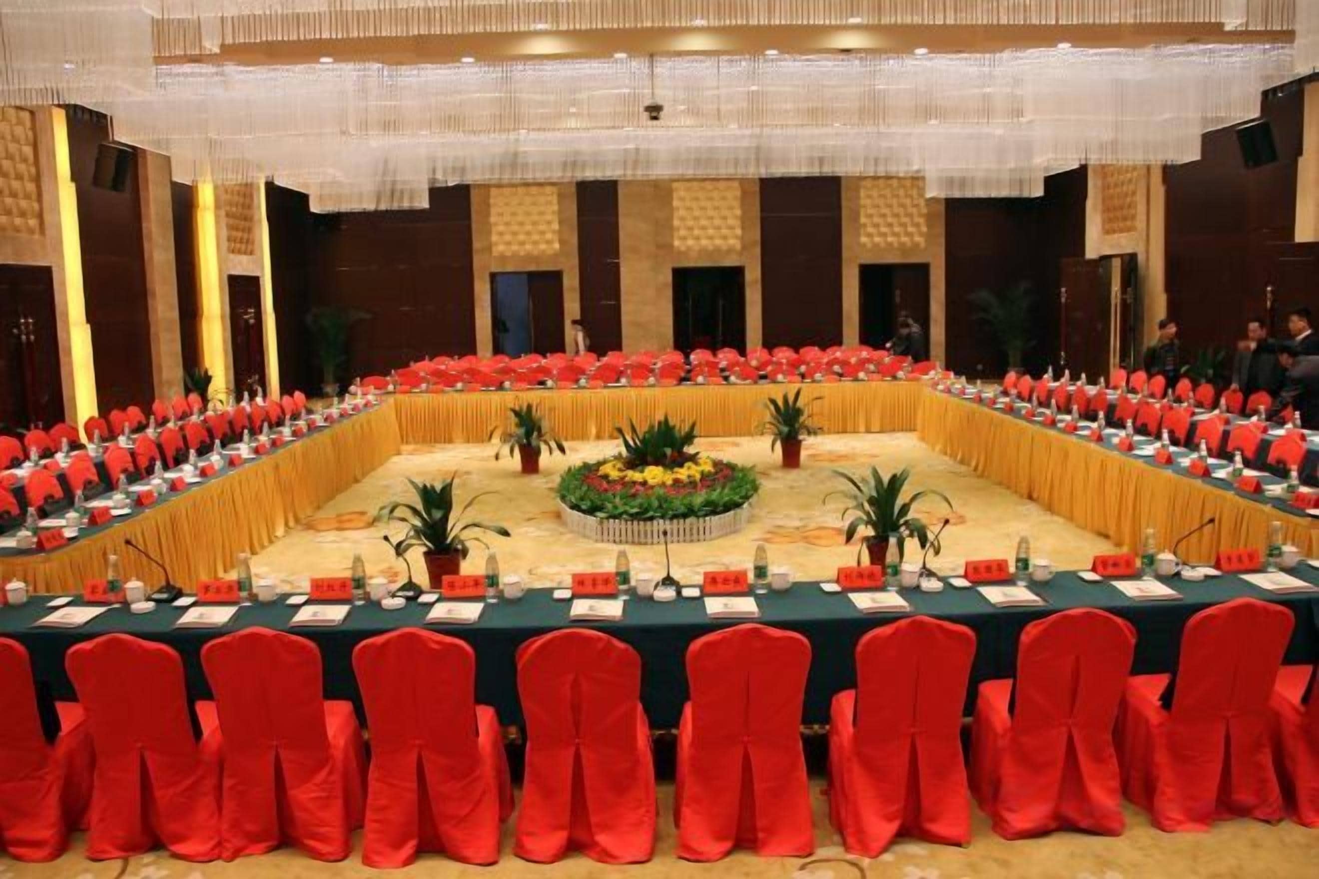 A conference room with a long table, red chairs, and a stage with a floral arrangement.