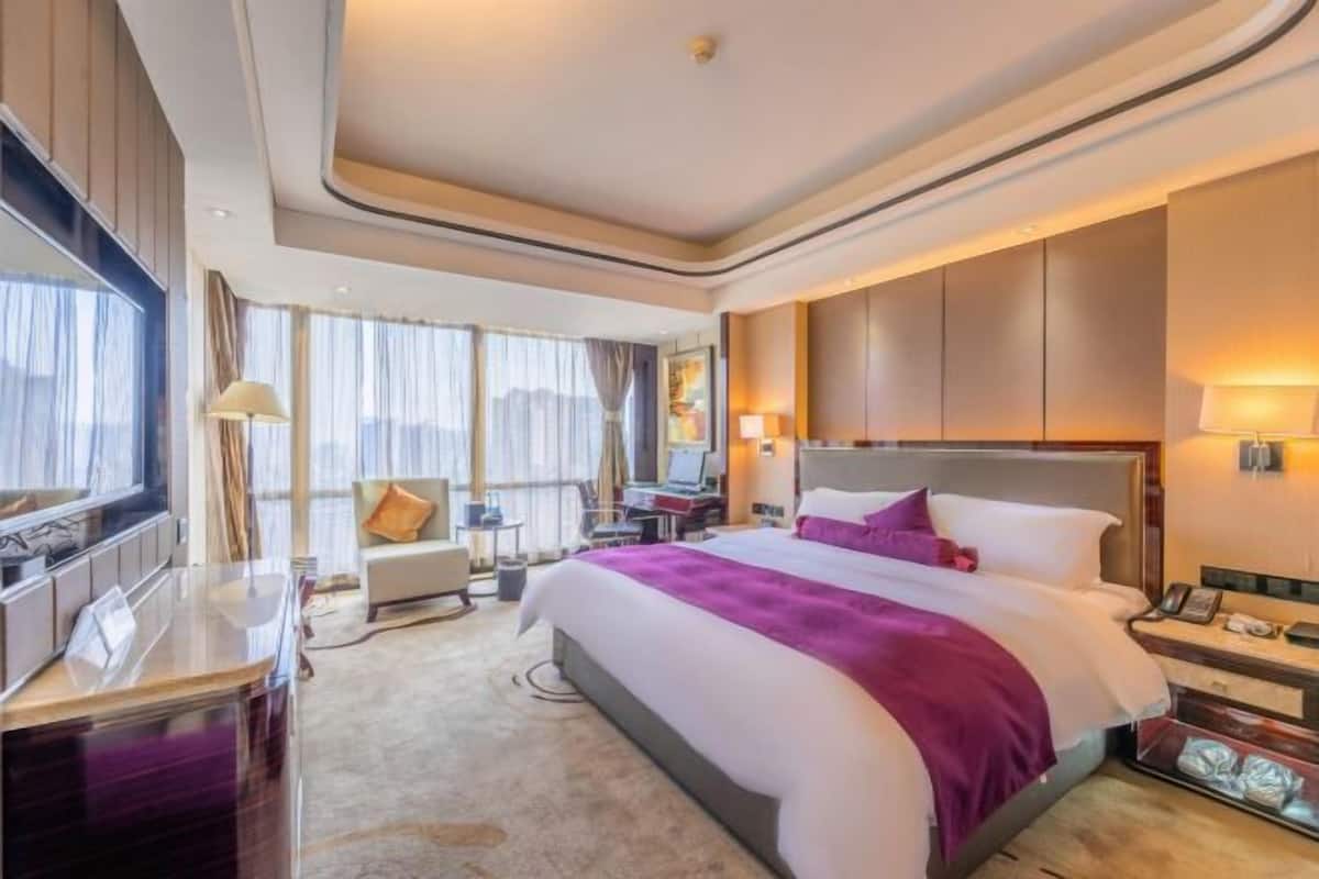 A hotel room with a large bed, a desk, a chair, and a TV.