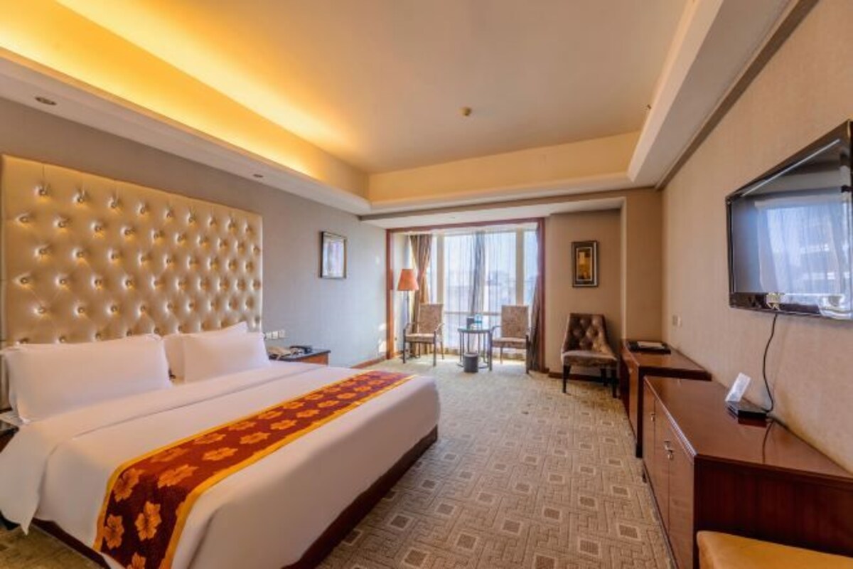 A hotel room with a large bed, a television, a desk, and a seating area with chairs.
