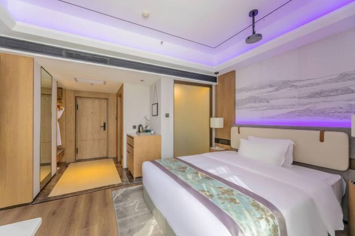 A modern hotel room with a large bed, a desk, and a wardrobe.