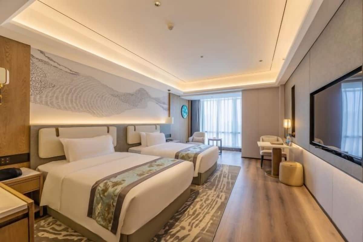 A hotel room with two beds, a large wall mural, a television, and a seating area with a view of the outdoors.