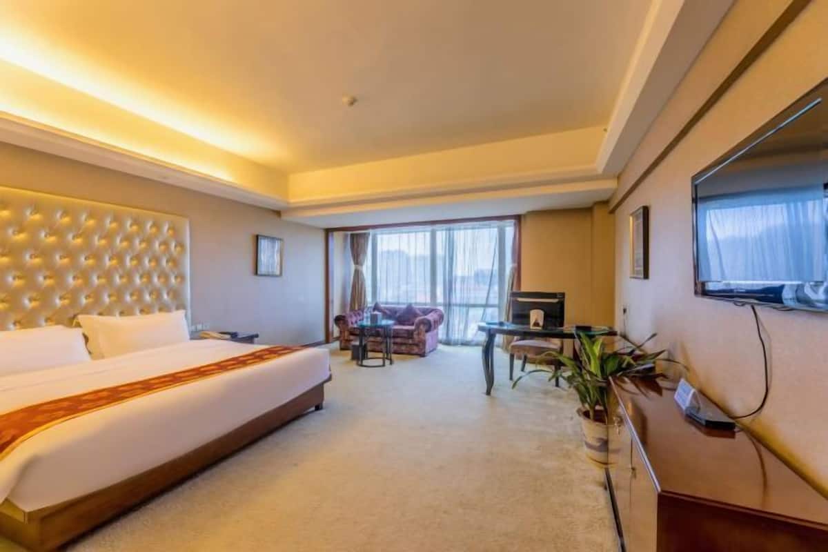 A hotel room with a large bed, a sofa, a desk, and a TV.