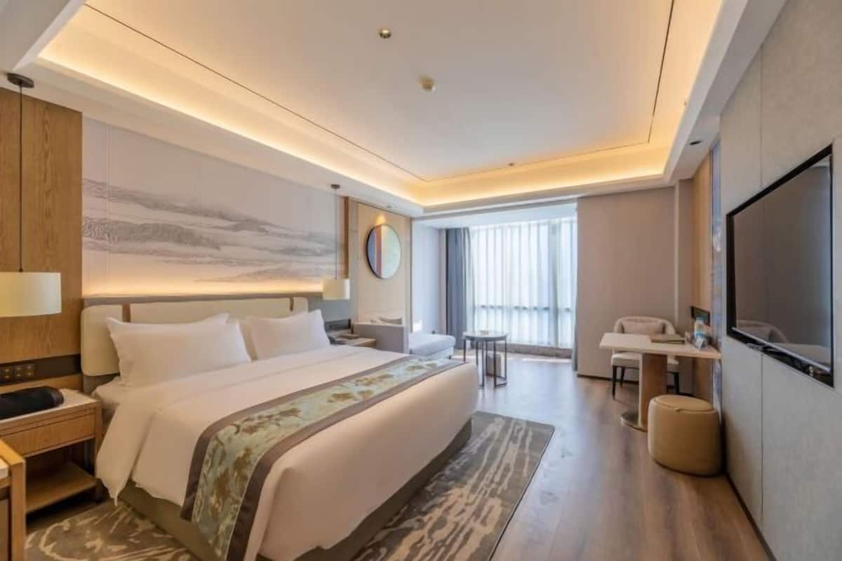 A modern hotel room with a large bed, a desk, a TV, and a view of the outdoors.