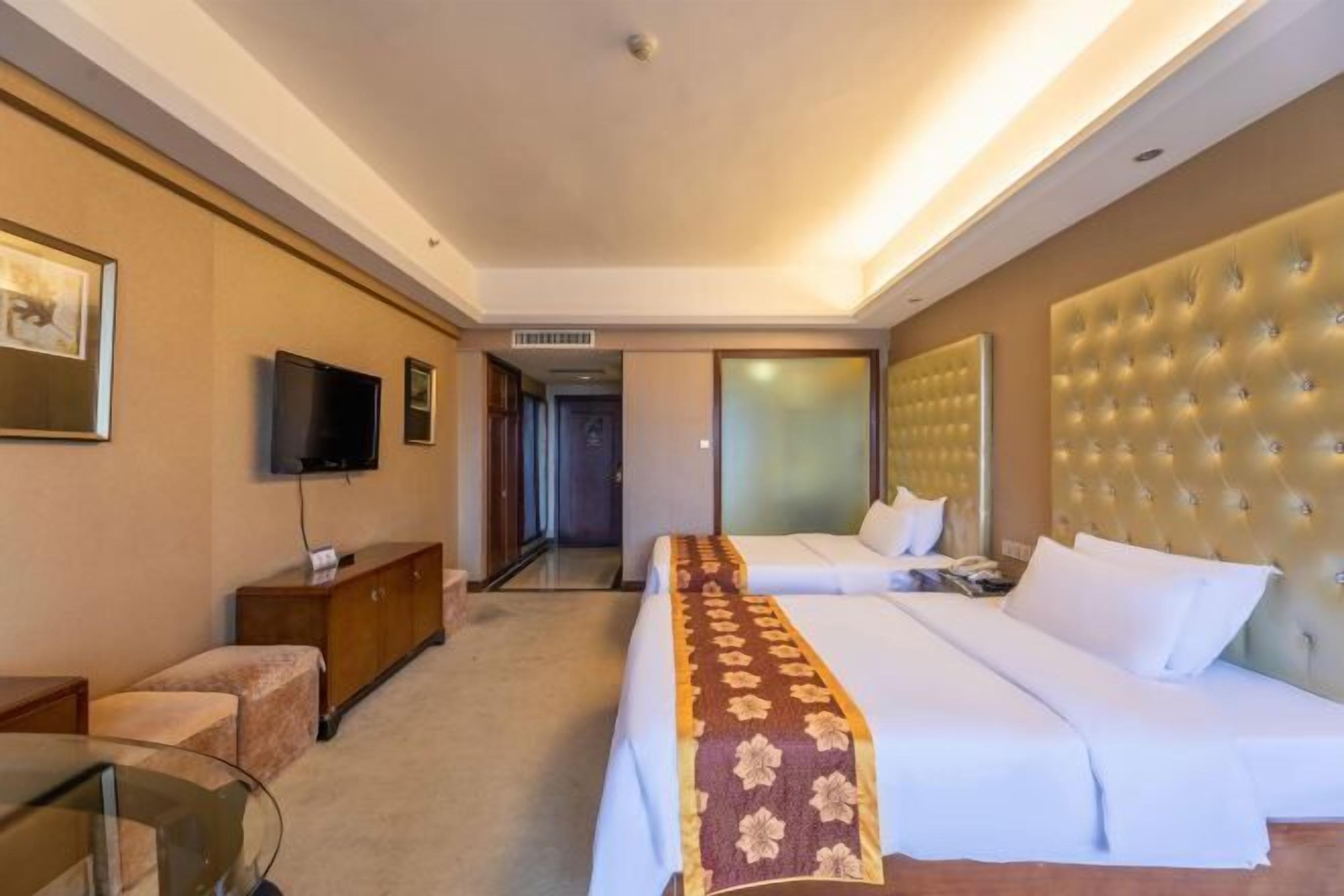 A hotel room with two beds, a television, a desk, and a minibar.